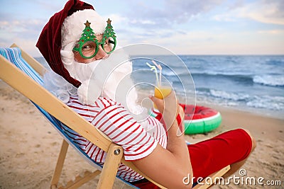 Santa Claus in party glasses with cocktail relaxing on beach. Christmas vacation Stock Photo