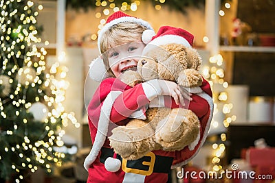 Santa helper. Surprised Little Santa boy in embrace teddy bear. Stock Photo