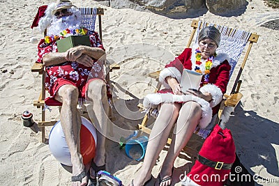 Santa and Mrs Claus reading books and napping on beach Stock Photo