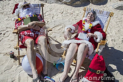 Santa and Mrs Claus sleeping with books on beach Stock Photo