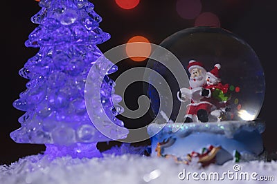 Santa near a beautiful, colourful, New Year`s fir-tree, sits in a glass sphere and prepares gifts for children for new year Stock Photo