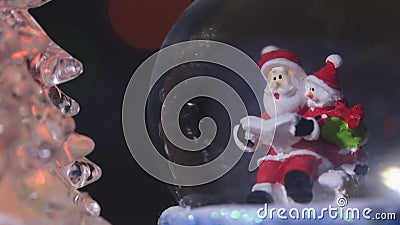 Santa near a beautiful, colourful, New Year`s fir-tree, sits in a glass sphere and prepares gifts for children for new year Stock Photo