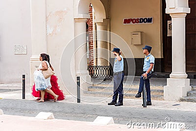 SANTO DOMINGO, DOMINICAN REPUBLIC - AUGUST 8, 2017: Two women in beautiful dresses and policemen in a city street. Copy space for Editorial Stock Photo