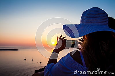 Young woman taking pictures of the beautiful sunset at the famous Caldera of Santorini Island in Editorial Stock Photo