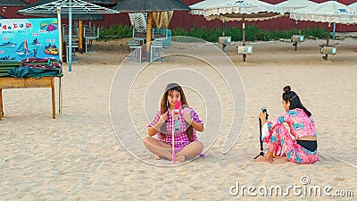 Two young Chinese girls on the beach, sitting on the sand, take a selfie Editorial Stock Photo