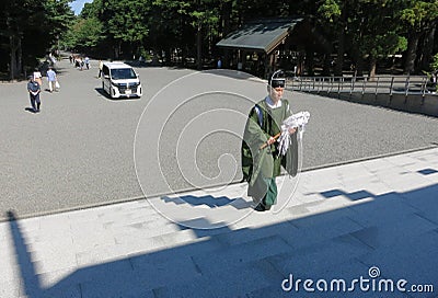 A shinto priest wearing a green garment walks up the stairs of a shrine after blessing a new car Editorial Stock Photo