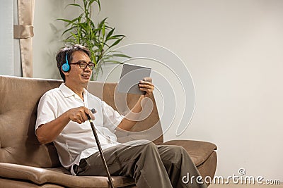 Sarcopenia older man is using digital tablet and headphone on sofa for relax at nursing home Stock Photo