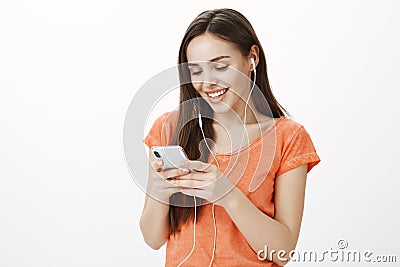 Satisfied attractive timid girl in earbuds, listening music, picking favorite track in smartphone playlist, smiling Stock Photo
