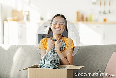 Satisfied buyer concept. Overjoyed asian woman opening and unboxing package after delivery, hugging shirt Stock Photo
