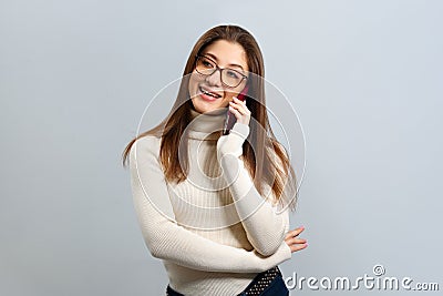 A satisfied girl in glasses talks on a mobile phone on a light gray background. Young woman with loose hair smiling Stock Photo