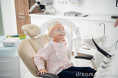 A satisfied little dentist patient showing her perfect smile after dental treatment in a clinic. A box with medical Stock Photo