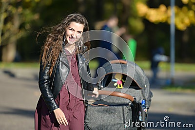 Satisfied mom on a walk with a stroller. Young mother walking with baby in the park. Beautiful smile and uplifted mood, satisfied Stock Photo