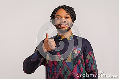 Satisfied pleased african man with dreadlocks showing thumbs up with toothy smile on face, happy with good service, like and Stock Photo