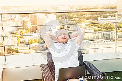 Satisfied with work done. Cheerful young man holding hands behind head and keeping eyes closed while sitting on the terrace with U Stock Photo