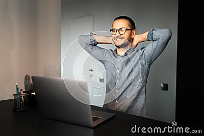 Satisfied with work done. Happiness young business man relaxing. Working home at laptop. Wearing eyeglasses and shirt. Background Stock Photo
