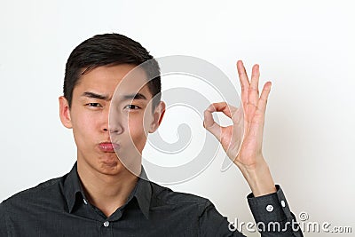 Satisfied young Asian man giving the okay sign and looking at ca Stock Photo