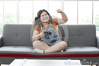 Satisfy chubby woman play video games at home and raised hand for joyful or mission complete Stock Photo