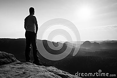 Satisfy tall hiker in grey shirt and dark trousers. Sprtsman on the peak of sharp rock edge watching down to landscape. Stock Photo