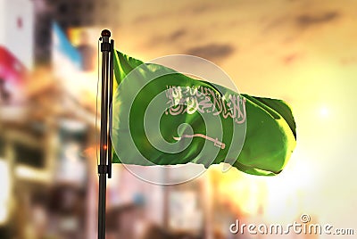 Saudi Arabia Flag Against City Blurred Background At Sunrise Backlight Stock Photo