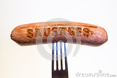 Sausage with an inscription pinned on a fork, on a white background. Stock Photo