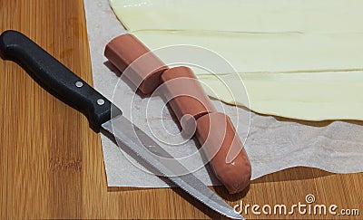 Sausage, puff pastry and knife on a wooden cutting board. Stock Photo