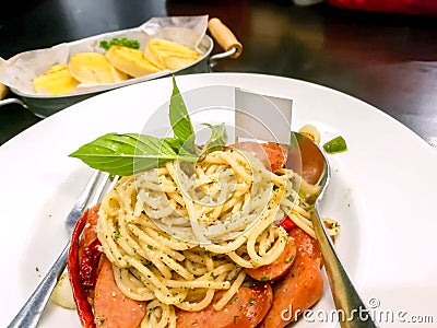 Sausage spaghetti in Thai style on white ceramic plate with spoon and fork and garlic bread in aluminium plate Stock Photo