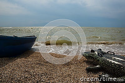 Saver boat and big inflatable toy crocodile shape lie in front of sea on beach line. Stock Photo