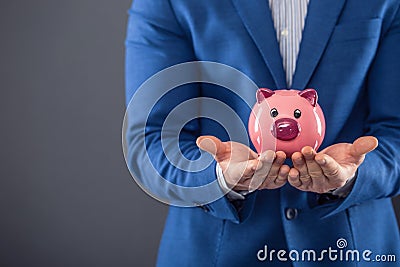 Saving money. Businesman holding pink piggy and putting coin into piggy bank Stock Photo