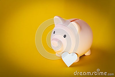Saving money. The hand puts a heart in a piggy bank. Salary retention. Stock Photo