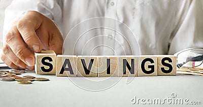 SAVINGS inscription on the texture of wooden cubes. A business man holds a cube in his hand. An inscription on a financial, Stock Photo