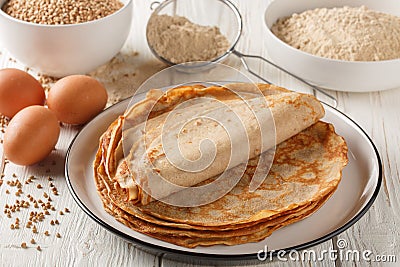 Savory crepes Buckwheat Galettes closeup on a plate with ingredients flour, cereal and eggs closeup on the wooden table. Stock Photo