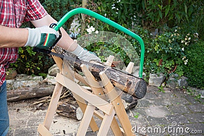 Sawing firewood manually with a hacksaw on a wooden sawhorse Stock Photo