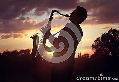 Saxophonist playing sax against sunset Stock Photo