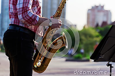 Saxophonist plays a golden saxophone on the street with passers-by in sight. spring. musical reed wind instrument. tongue wooden Stock Photo