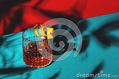 Sazerac, classic alcoholic cocktail with cognac, bourbon, absinthe, bitters, sugar and lemon zest. Dazzling red blue background Stock Photo