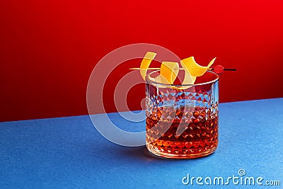 Sazerac cocktail with cognac, bourbon, absinthe, bitters, sugar and lemon peel. Dazzling red blue background with hard light and Stock Photo