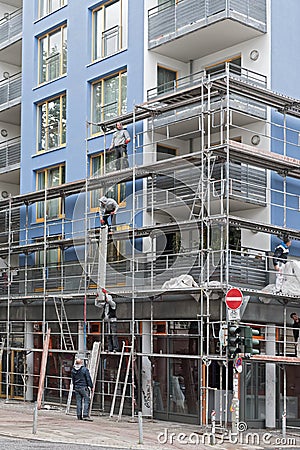 Scaffolding builders assemble a scaffolding in front of a blue house Editorial Stock Photo