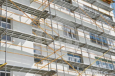 Scaffolding near a new house, building exterior, construction and repair industry, white wall and window, yellow pipe Stock Photo