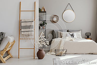 Scandi open space bedroom interior with bed with knit blanket and many pillows, rack with books and decor, carpet on the Stock Photo