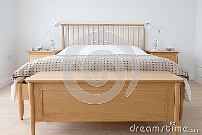 Scandinavian inspired bedroom interior showing wooden bedroom furniture, white painted walls, white bedding and colourful blanket Stock Photo