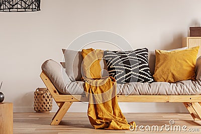 Scandinavian sofa with pillows and dark yellow blanket in bright living room interior with black chandelier Stock Photo