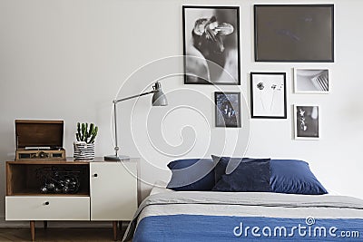 Scandinavian style, wooden dresser by a navy blue bed and framed art gallery on a white wall of a creative bedroom Stock Photo