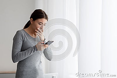 Scared anxious upset sad caucasian young female reads bad message on smartphone and afraid at home alone Stock Photo