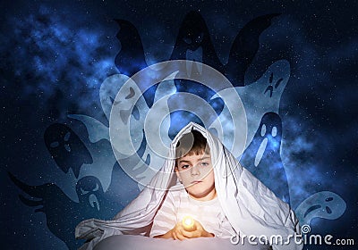 Scared boy with flashlight under blanket Stock Photo