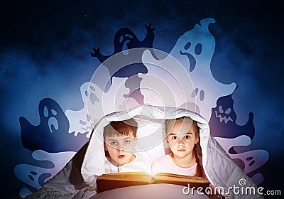 Scared girl and boy reading book in bed Stock Photo