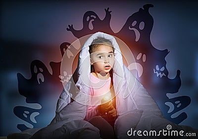 Scared girl with flashlight under blanket Stock Photo