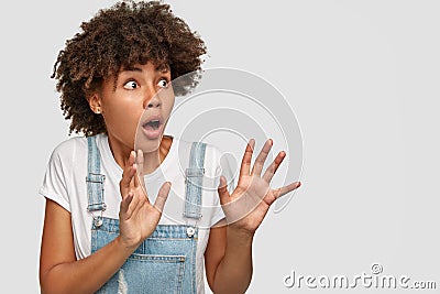 Scared horrified dark skinned lady keeps breath, hands in protective gesture, notices something awful, afraids of Stock Photo