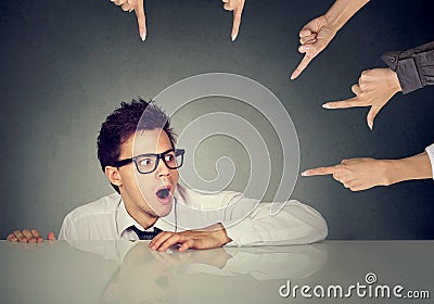 Scared man employee hiding under the table being accused by people who point fingers at him Stock Photo