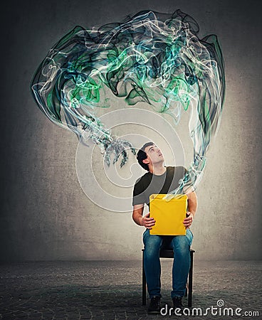 Scared man seated on a chair holding mystery box on knees looking up with shocked expression as a mystic dark smoke comes out of Stock Photo