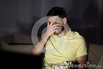 Scared man watching tv and eating popcorn at night Stock Photo